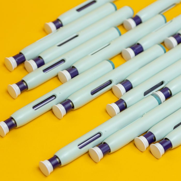 Slanted grouping of self application syringe pens on seamless yellow background. Studio medical equipment still life concept with auto-injector disposable devices.