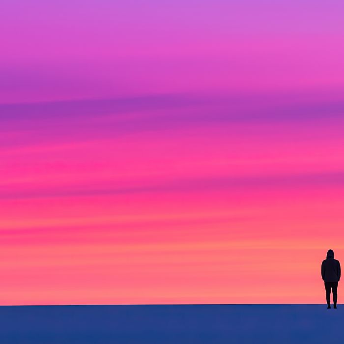 A solitary figure stands on a vast landscape, illuminated by a vibrant pink and purple sunset sky.